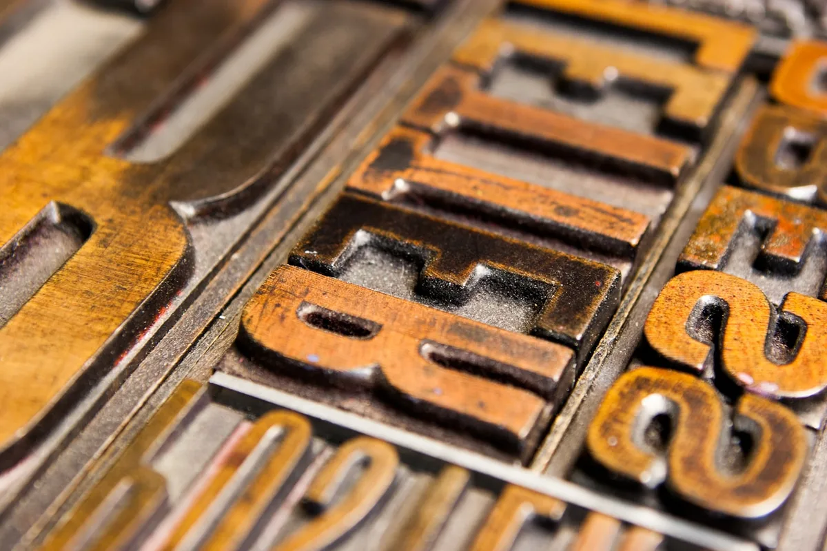 Antique letterpress type blocks in warm gold-toned wood, letters and numerals set in a tray